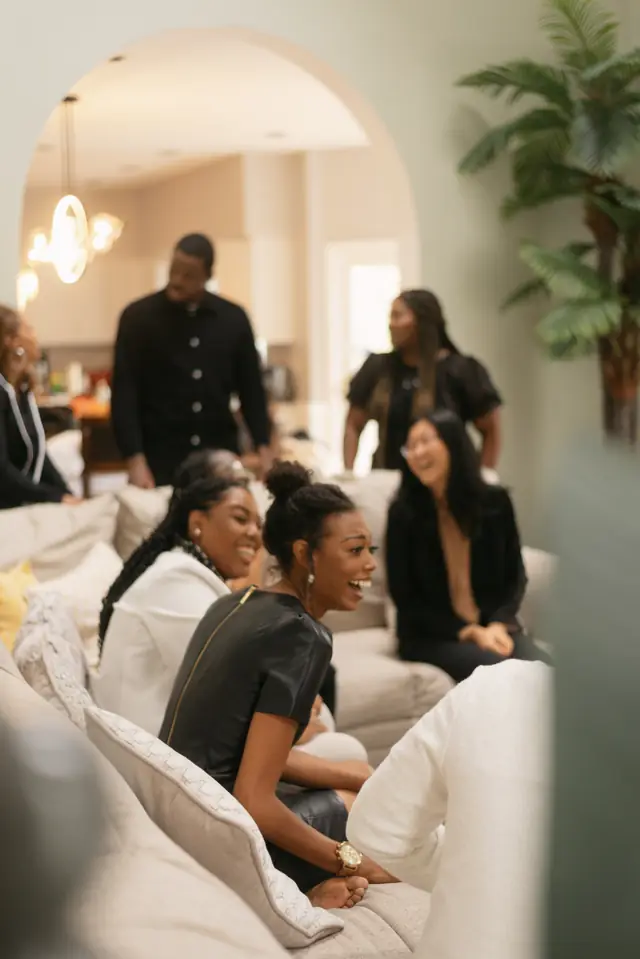 Seen through an arched doorway, women laugh together on a sofa.
